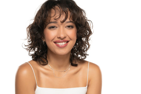 Young dark skinned smiling woman with makeup and wavy hair posing on a white studio backgroundの写真素材