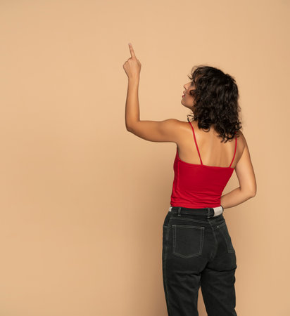 Young dark skinned woman pointing at something on a beige studio backgroundの写真素材