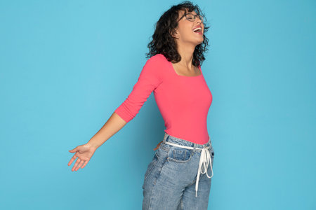 Young happy exotic brunette woman in pink blouse and rope belt jeans posing on a white studio background. Side view.の写真素材