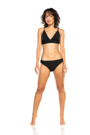 Young smiling exotic brunette woman in black bikini swimsuit posing on a white studio background. Front view.の写真素材