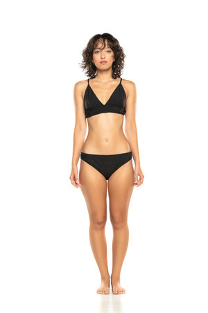Young exotic brunette woman in black bikini swimsuit posing on a white background. Front view.の写真素材