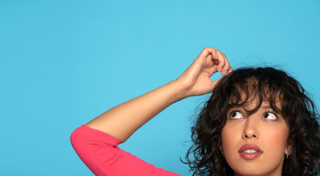 closeup portrait headshot of cute puzzled exotic woman looking up isolated on blue studio wall background with copy space above head.の写真素材
