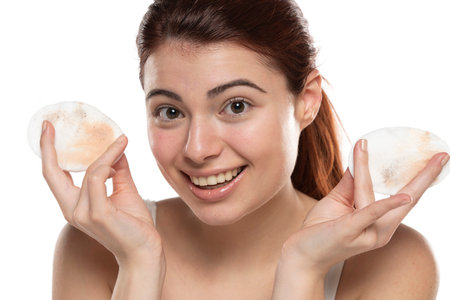 young redhead woman shows a dirty cotton pad of cotton from cleaning her makeup on a white studio backgroundの写真素材