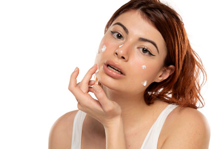 Beauty portrait image of pretty redhead woman applying face cream isolated over white studio backgroundの写真素材