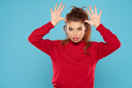 Woman in red blouse mocking someone sticking her tongue out on a blue studio backgroundの写真素材