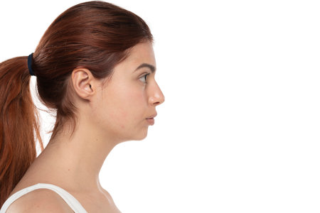 profile of a young serious redhead woman without makeup with long hair on a white studio backgroundの写真素材