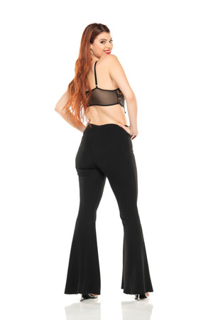 Fashion style studio portrait of beautiful young woman. Black wide leg pants and black lace bra. Model standing and posing against white studio backgroundの写真素材
