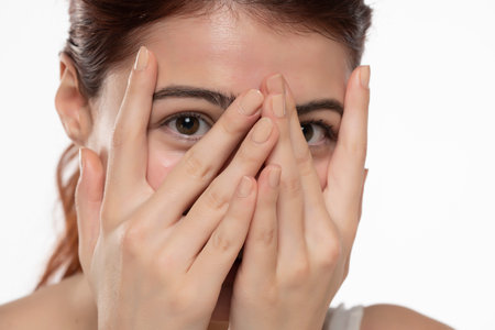Portrait of yong happy ashamed woman, covering face with hands, beautiful model posing in studio over white background.の写真素材