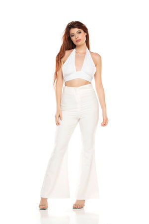 Fashion style studio portrait of beautiful young woman. White wide leg pants and white sleevles shirt. Model standing and posing against white studio backgroundの写真素材