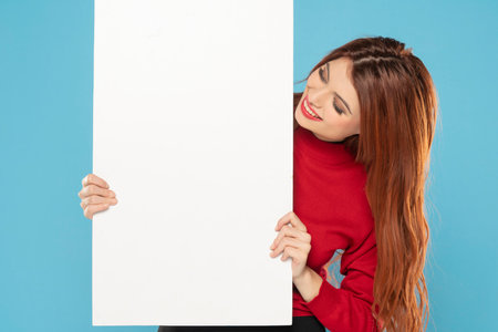 Banner of young happy redhead woman feeling happiness and holding Empty white canvas frame for text or advertising isolated on blue studio backgroundの写真素材
