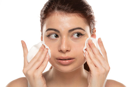 Beautiful redhead woman cleaning her face with cotton swab over white studio backgroundの写真素材