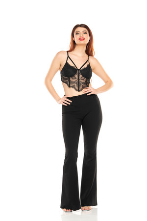 Fashion style studio portrait of beautiful young woman. Black wide leg pants and black lace bra. Model standing and posing against white studio backgroundの写真素材