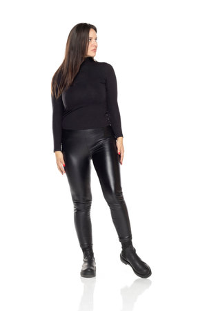 Front view of a young woman in tight leather pants and boots on a white studio backgroundの写真素材