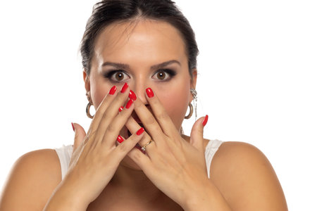 Surprised woman covering with hands her mouth on a white studio backgroundの写真素材