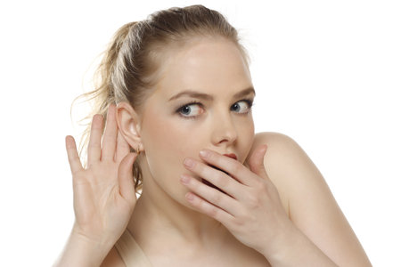 Young caucasian shocked blonde woman listening to something by putting hand on the ear on a white studio backgroundの写真素材
