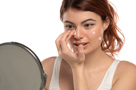 Beauty portrait image of pretty redhead smiling woman applying face cream isolated over white studio backgroundの写真素材