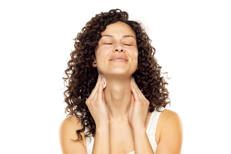 Skincare Concept. Attractive Curly Woman Clean Her Neck Using Cotton Pad Cleansing Face Skin Over White Studio Background.の写真素材