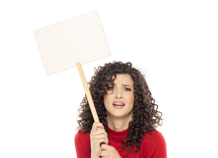 Young curly unhappy woman holding blank sign on white studio background.の写真素材