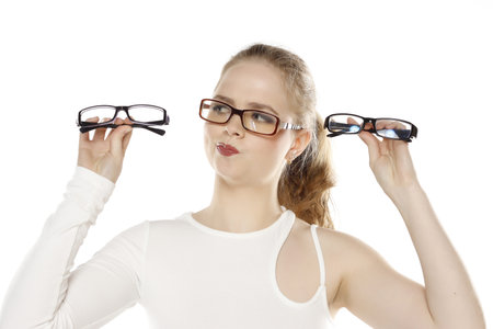 a young doubtful blonde woman chooses a frame for her new glasses on white studio background