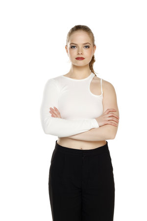 Front view of young blond woman in trousers and white blouses posing with arms folded on white studio backgroundの写真素材
