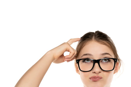 Expressive Beauty: Portrait of a Surprised Young Woman with Makeup and Glasses, Updo, Hair-Scratching and Raised Eyebrows on White Studio Backgroundの写真素材
