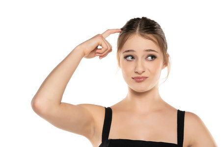 Expressive Beauty: Portrait of a Surprised Young Woman with Makeup, Updo, Hair-Scratching and Raised Eyebrows on White Studio Backgroundの写真素材