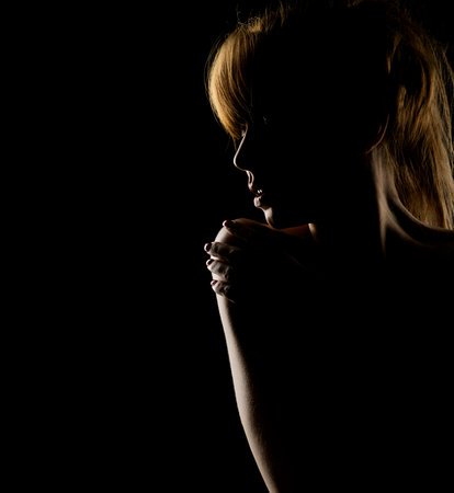 Silhouette of a young woman  touching her shoulder on a black studio backgroundの写真素材