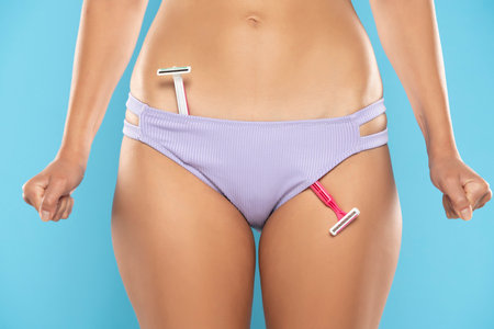 shaving blades in panties. girl health and intimate hygiene. Beautiful Woman's body with smooth soft skin in blue bikini panties with nervous fists. Epilation Concepts. blue studio backgroundの写真素材