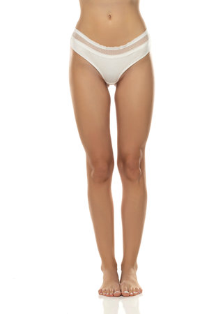 woman's legs are elegantly posed, showcasing white panties from the front on white studio background.Femininity, sensuality, and body positivity, making it suitable for various themes in the lingerie, beauty industry.の写真素材