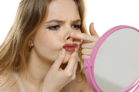 worried young blond woman in front of the mirror touches her mouth and nose on a white studio backgroundの写真素材