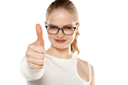 Smiling woman with glasses showing thumb up on a white studio backgroundの写真素材