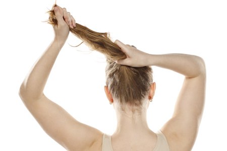 Back,  rear view of a young blond woman tying her long hair on a white studio backgroundの写真素材