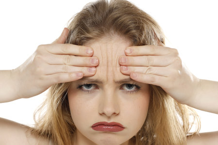 portrait of a young unhappy woman showing her wrinkles on her forehead on a white studio backgroundの写真素材