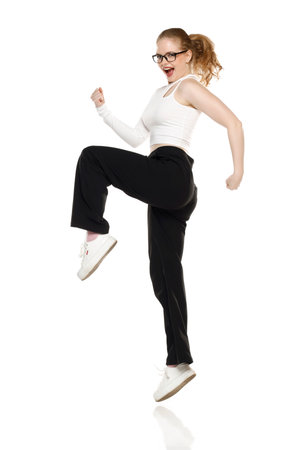 Portrait, success and a ypung woman jumping isolated on a white studio background in celebration of achievement. Freedom, motivation and energy with a winning gestureの写真素材
