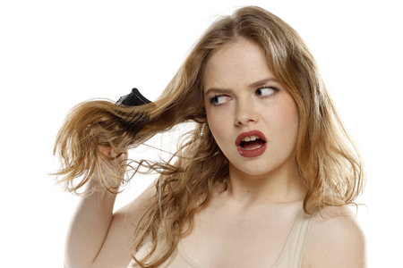 Beautiful blonde unhappyu woman brushing hair with comb on a white studio backgroundの写真素材