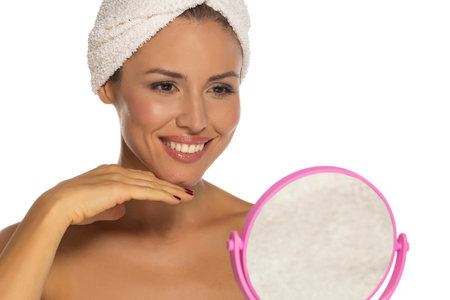 Happy confident young lady with towel on head look in the mirror touching moisturized soft healthy sensitive skin doing morning hydration spa beauty routine, facial skincare treatment conceptの写真素材