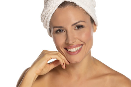 Beauty portrait of a cheerful attractive half naked woman with a towel wrapped around her head with toothy smile and looking at camera isolated over white studio backgroundの写真素材