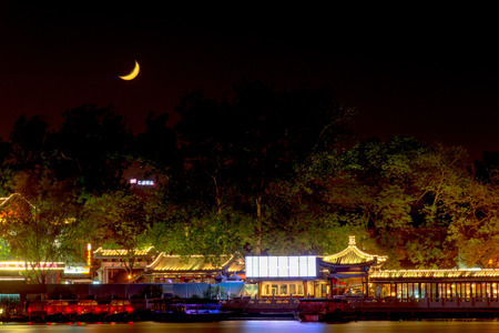Night city and pier. Night city lights reflected in the water. The moon in the sky at night and trees at the pier with lightsのeditorial素材