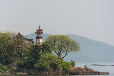 The lighthouse on the shores of the calm water. Lighthouse on the land on the background of water and land. Old, ancient lighthouse in the Chinese, asia styleの写真素材