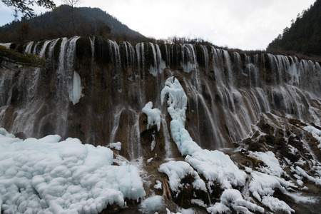 Waterfall in the forest. Frozen water drains over the rocks. The rock is covered with moss on which cold water flows.の写真素材