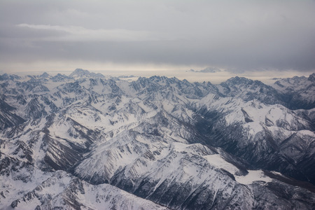 View of the mountains covered with snow from the airplane. Mountains to horizon. Mountain range in cloudy weatherの写真素材