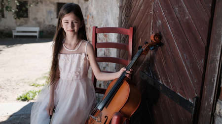 beautiful girl in a pink dress sits on a red chair with a celloの写真素材