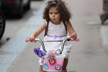 little curly girl rides a bicycle on a city street.の写真素材