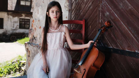 beautiful girl in a pink dress sits on a red chair with a celloの写真素材