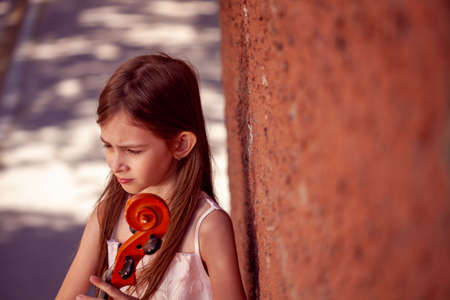 beautiful girl in a pink dress stands with a cello in the city against the wallの写真素材