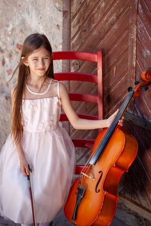 beautiful girl in a pink dress sits on a red chair with a celloの写真素材