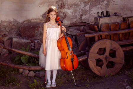 beautiful girl in a pink dress with a cello in the villageの写真素材