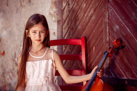 beautiful girl in a pink dress sits on a red chair with a celloの写真素材