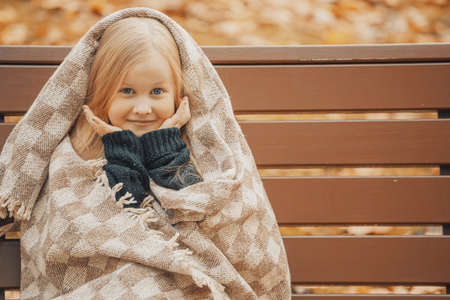 little blonde girl in a plaid in the park on a benchの写真素材