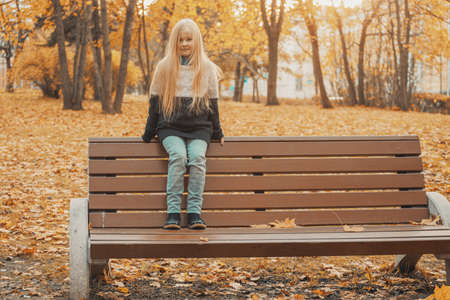 beautiful little blonde girl in the park in autumnの写真素材